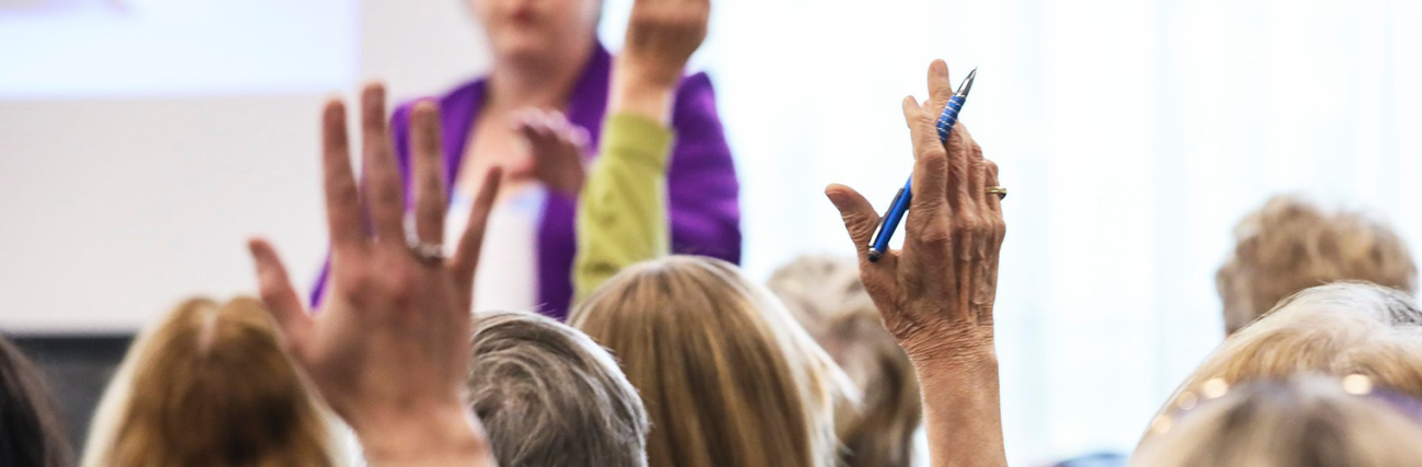 Image depicts a community networking event with a cropped in focus around hands being raised